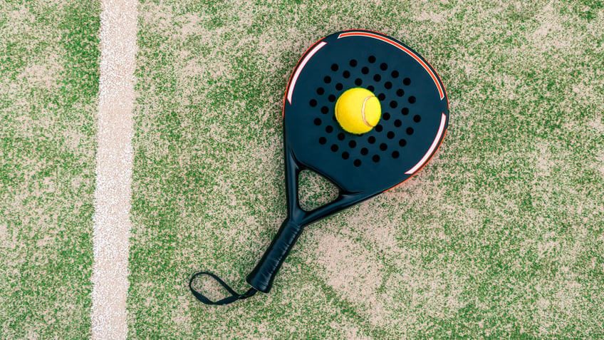 Yellow ball on top of the padel racket and behind net on gre